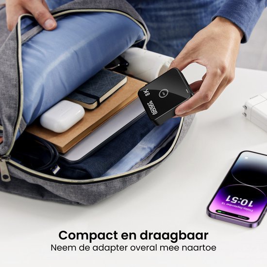 Hand plaatst compact zwart apparaat in grijze tas met laptop, notitieboek en oplaadkabels