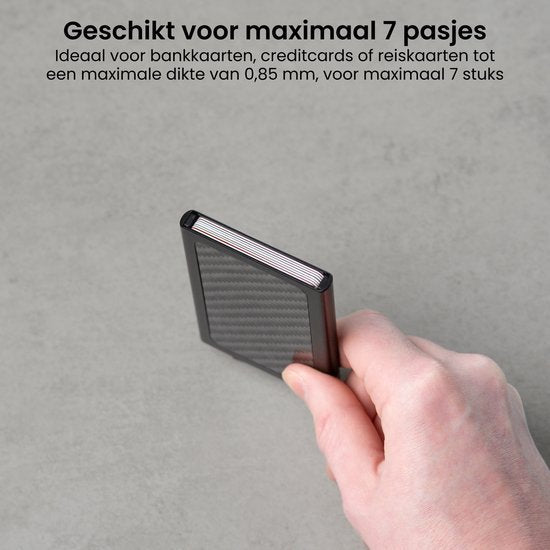 Hand die een compact zwart kaartetui met carbontextuur vasthoudt tegen een grijze achtergrond