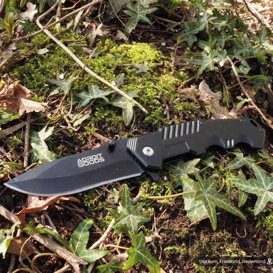 vouwmes met zwarte kunststof handgreep ligt op mos en bladeren in het bos