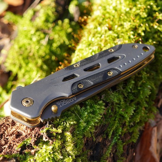 Inklapbaar mes met metalen en zwarte details liggend op groene mosgrond in natuurlijk licht