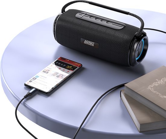 Zwarte draagbare Bluetooth-speaker met draagriem aangesloten op een smartphone op tafel