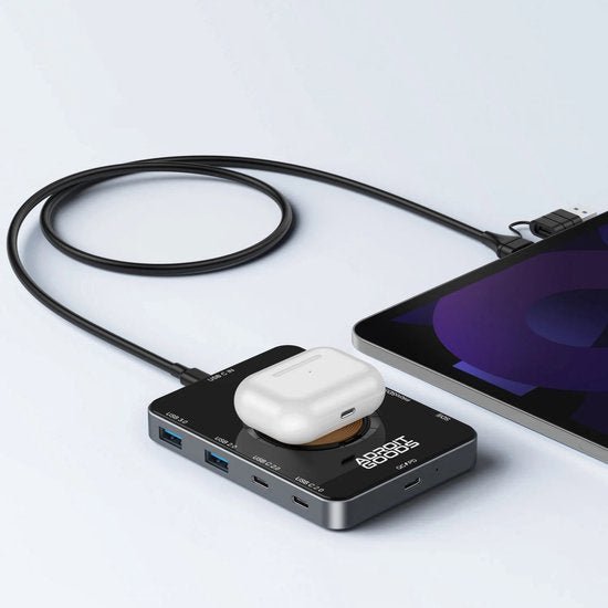 Zwarte USB-hub aangesloten op tablet met witte oplaadcase erop geplaatst, strak design.