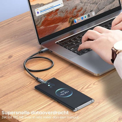 Hand die op laptoptoetsenbord typt, smartphone verbonden via kabel op houten tafel