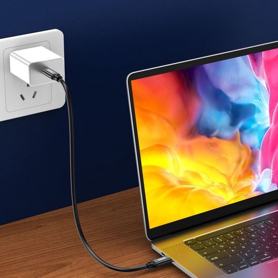 Laptop verbonden met een wit stopcontactlade via een zwarte oplaadkabel aan een houten tafel