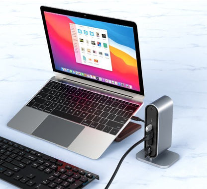 Laptop aangesloten op een compacte hub met meerdere poorten en een toetsenbord op marmeren oppervlak