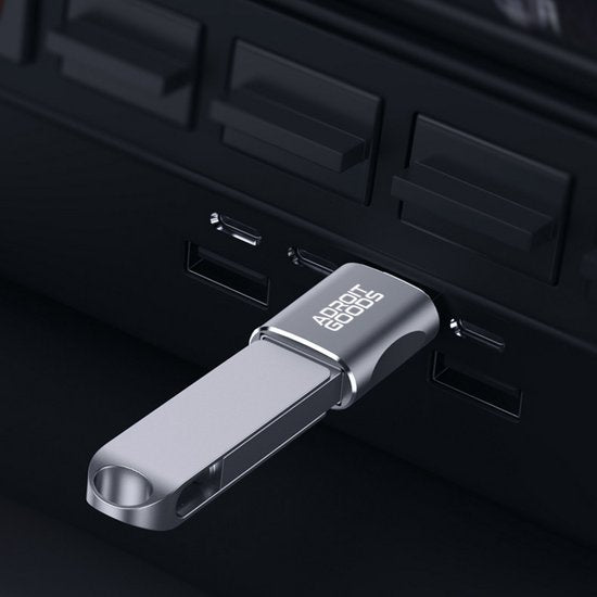 Zilverkleurige USB-stick met AdroitGoods logo aangesloten op zwarte laptoppoort.