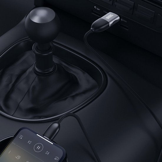 Zwarte versnellingspook met aangesloten kabel en telefoon in autointerieur close-up.