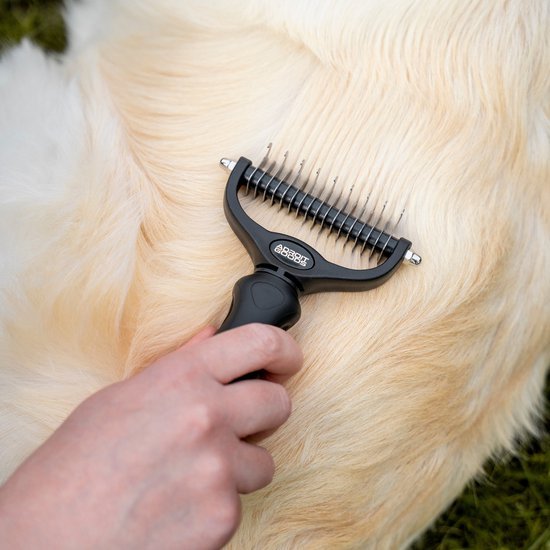 Hand gebruikt zwarte ontwarringskam op lichte, dikke vacht van een huisdier buiten