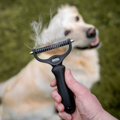 Close-up van een zwarte hondenborstel met opgehoopte witte hondenharen en een gouden retriever op de achtergrond