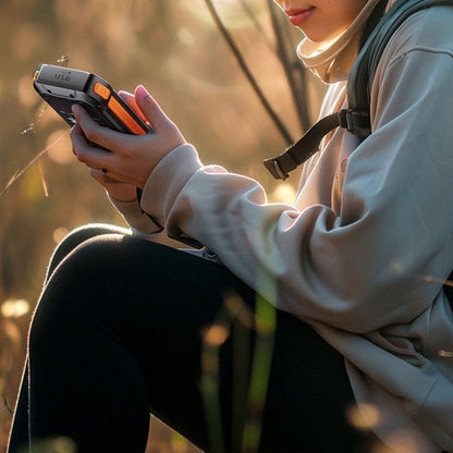 Vrouw zittend buiten met rugzak gebruikt een draagbaar apparaat in natuurlijk licht