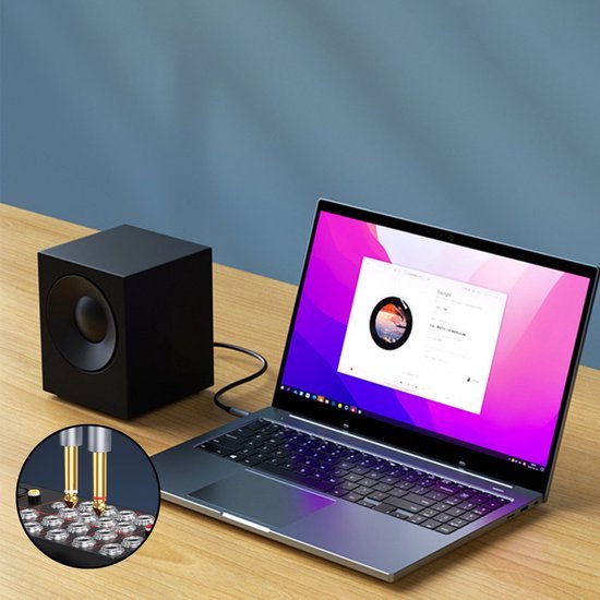 Zwarte kubusvormige luidspreker naast een laptop met muzieksoftware op een houten tafel