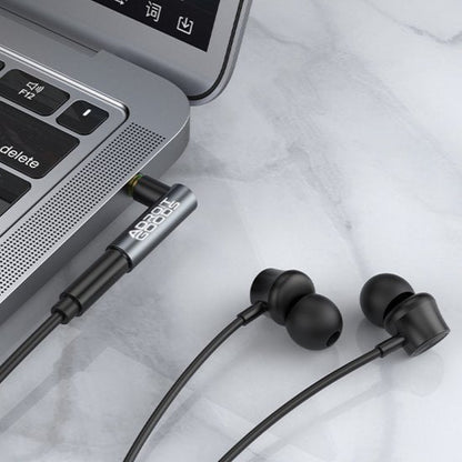 Zwarte oordopjes met kabel aangesloten op een laptop op een wit marmeren oppervlak.