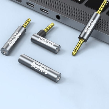 Vier metalen audio-adapters met 3,5 mm aansluiting naast een laptoppoort in grijze achtergrond