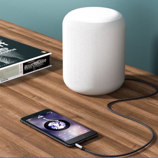 Wit cilindervormig draadloos speakerapparaat op houten tafel met verbonden smartphone.