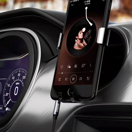 Telefoon gekoppeld aan autoradio met muziekspeler en zwart laadkabeltje in houder centraal op dashboard