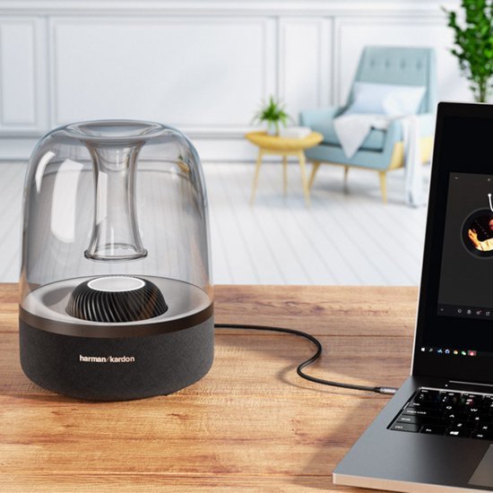 moderne transparante draadloze speaker met ronde basis op houten tafel naast laptop