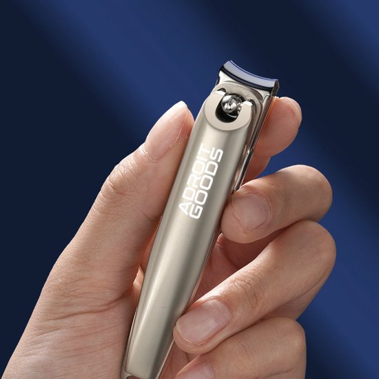 Hand houdt metalen nagelknipper met gravure Adroit Goods tegen een blauwe achtergrond