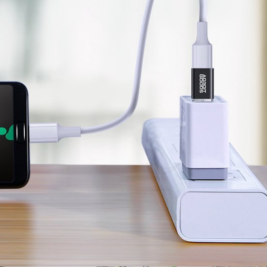 Wit oplaadkabel verbonden met telefoon en adapter in een stekkerdoos op houten oppervlak.