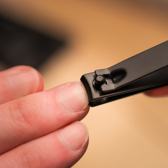 Hand die nagelknipper gebruikt om vingernagel te knippen met een neutrale achtergrond