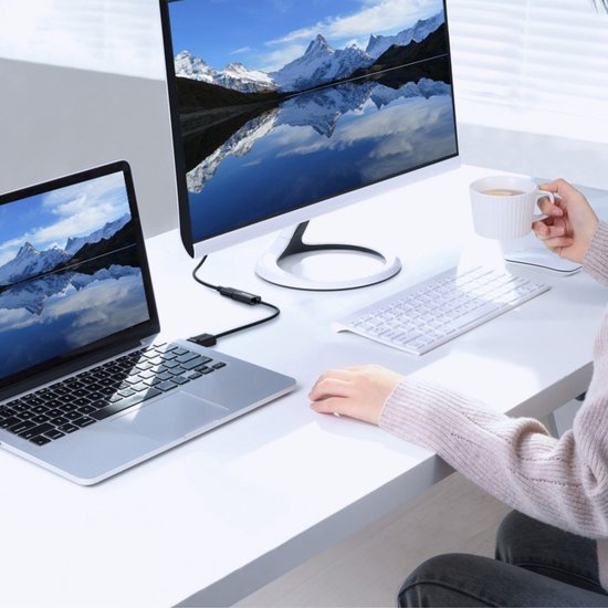 Laptop verbonden met een groot beeldscherm op een witte werkplek met toetsenbord en koffie