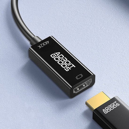 Zwarte AdroitGoods HDMI-verlengadapter met kabel en goudkleurige connector op een grijze achtergrond