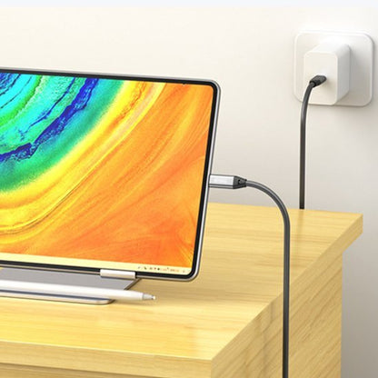 Tablet met usb-c-kabel verbonden aan oplader op een houten bureau in lichte omgeving