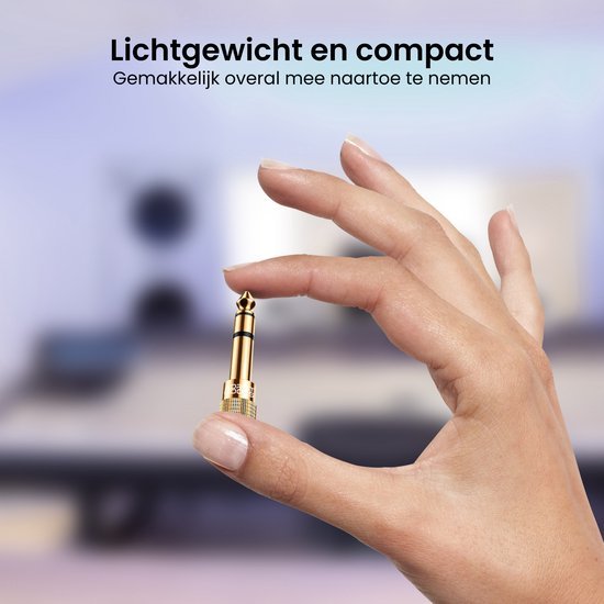 Hand die een klein goudkleurig audio-adapter stekkertje vasthoudt tegen een wazige achtergrond