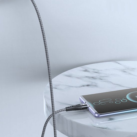 Flexibele oplaadkabel aangesloten op smartphone die op een marmeren tafel ligt