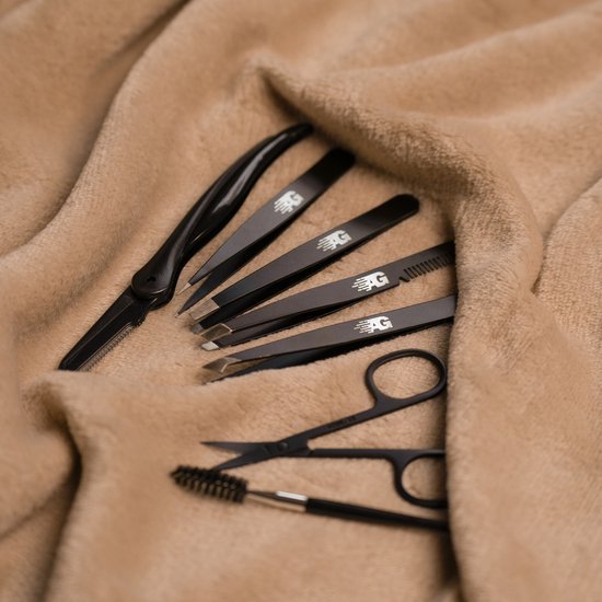 Zwarte professionele pincetten, schaar en borsteltje voor precisiewerk op zachte beige stof