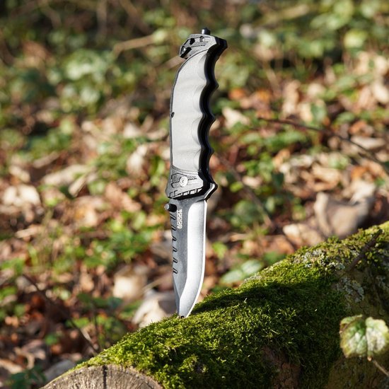 Vouwmes met zwarte handgreep en metalen lemmet, rechtop gestoken in met mos bedekt hout.