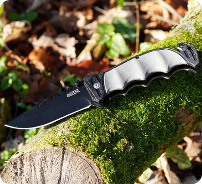 Opvouwbaar mes met zwarte lemmet en grijze antislip handgreep op mosbeslagen boomstam
