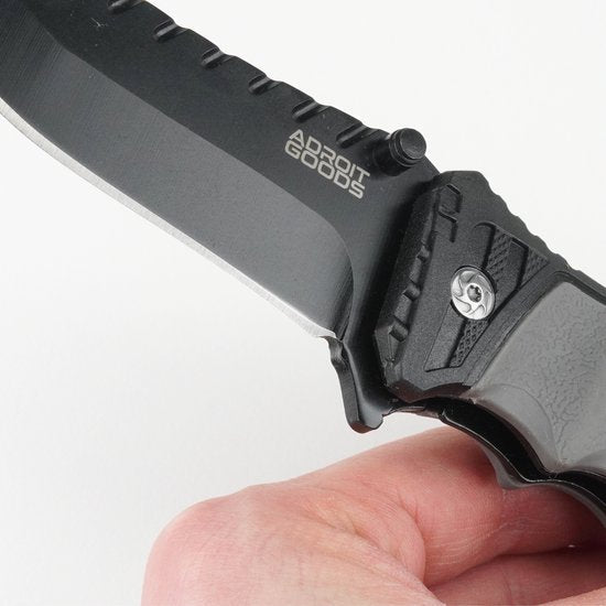 close-up van hand die een zwart mes met getande rug en AdroitGoods merk vasthoudt