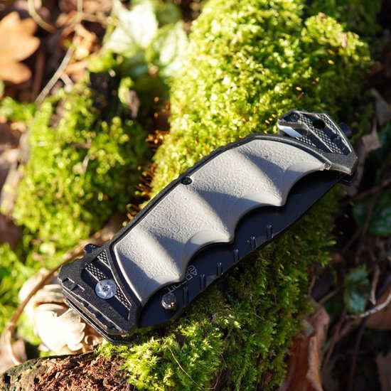 Zwart-grijs inklapbaar mes met ergonomisch handvat op groen mos in de natuur gelegen