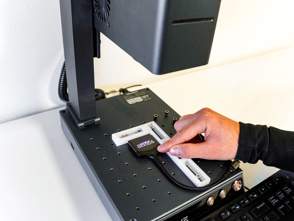 Hand plaatst een klein elektronisch onderdeel onder een apparaat op een zwart platform naast een toetsenbord