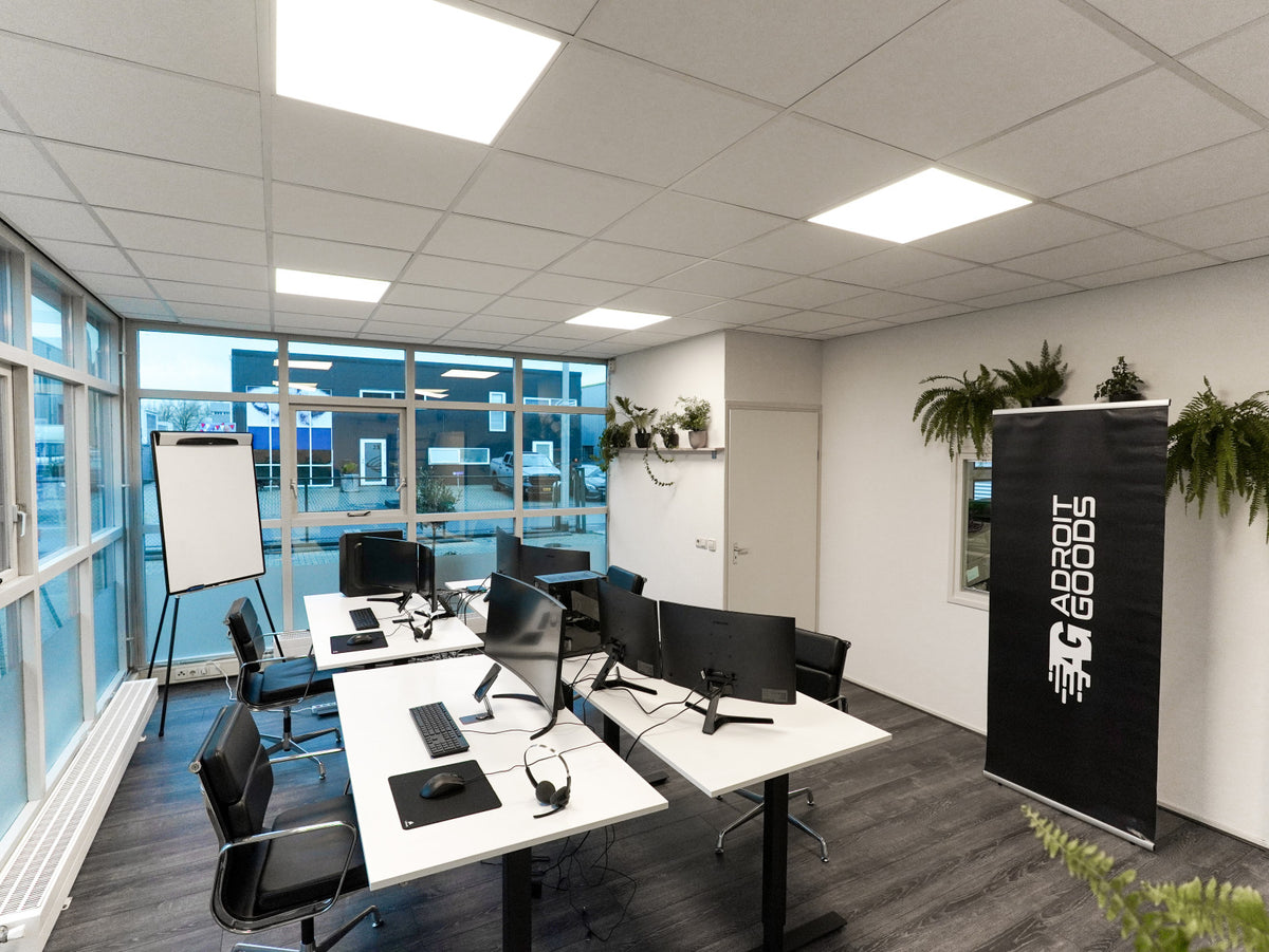 Moderne kantoorruimte met computers, bureaus, stoelen en een AdroitGoods banner.
