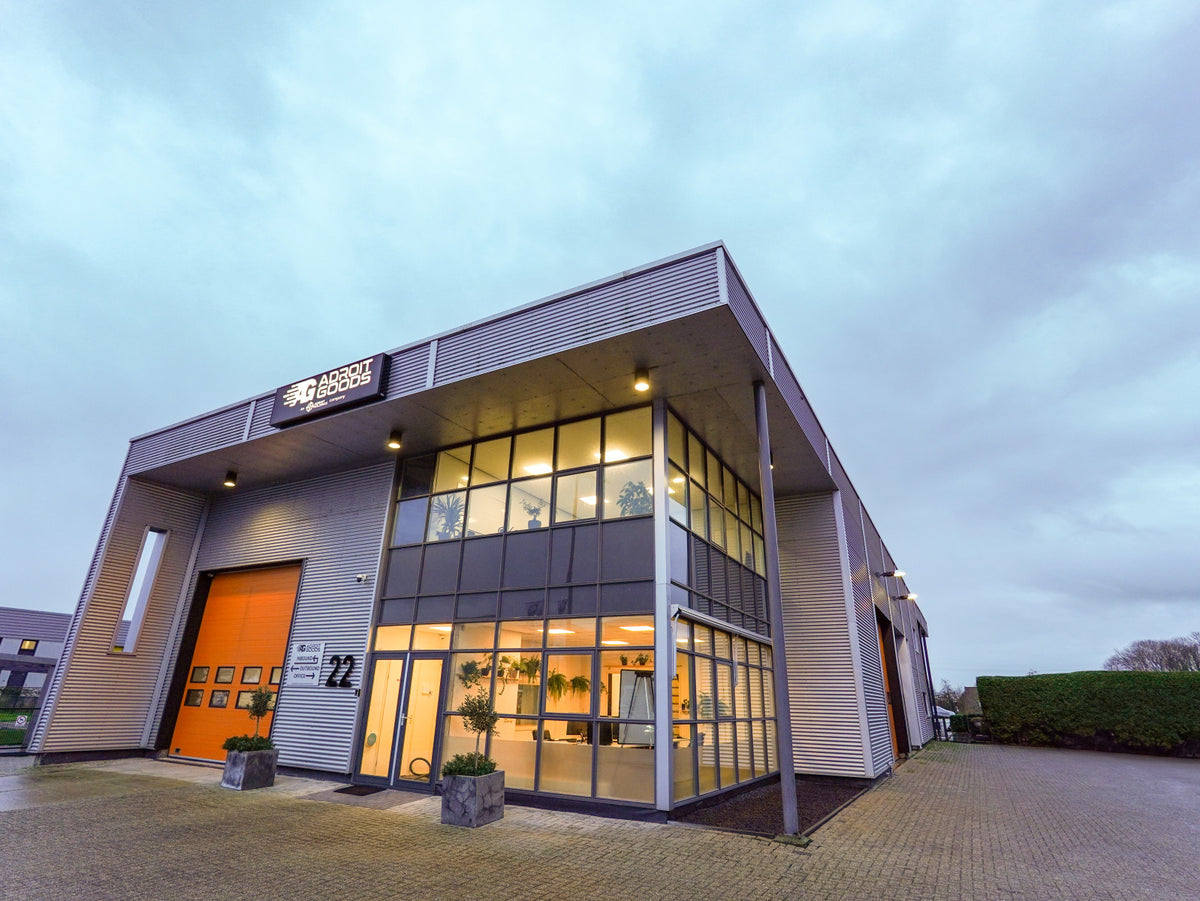 Moderne bedrijfsloods met groot raam en oranje overheaddeur bij bewolkte lucht