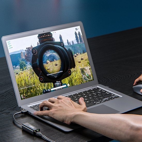 Hand met muis bedient laptop waarop een schietspel met vizier en landschap te zien is