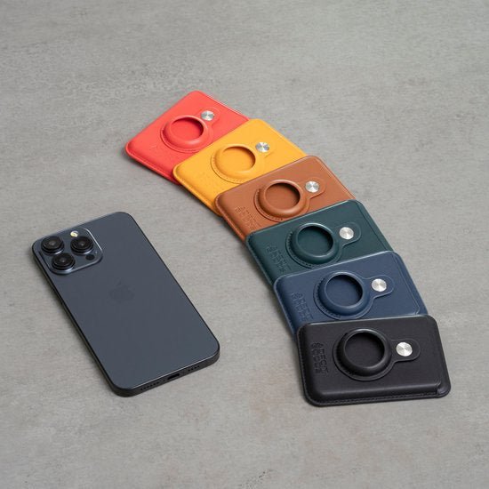 Zes leren portemonnees in verschillende kleuren met ronde houder naast zwarte smartphone op grijze achtergrond