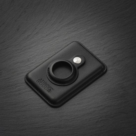 Zwart lederen kaarthouder met ring en metalen sluiting liggend op donkere steenachtige ondergrond