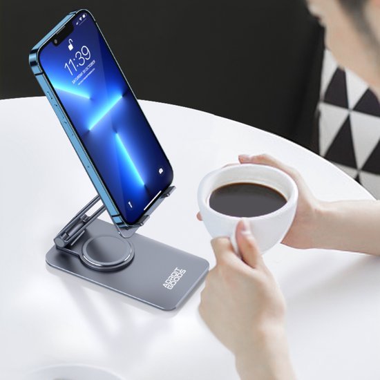 Smartphone op een grijze standaard met draadloze oplader naast handen die een kop koffie vasthouden