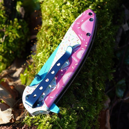 Gesloten zakmes met kleurrijk ijsje ontworpen handvat liggend op mosrijke ondergrond