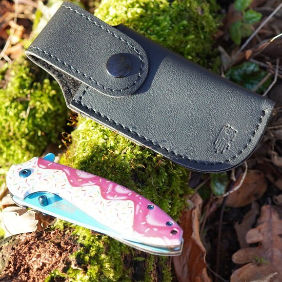 Zwart leren zakmeshoes met drukknop naast een roze en witte inklapbaar mes op mosgrond