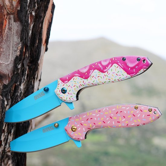 Twee kleurrijke zakmessen met blauw lemmet en handvatten in roze met spikkels, tegen boom en natuur achtergrond