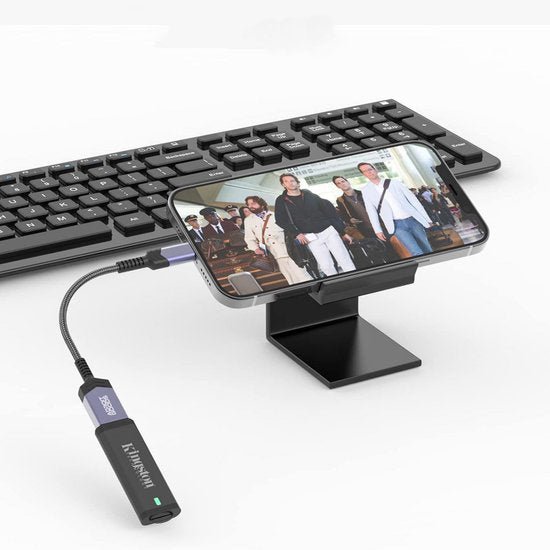 Telefoon op standaard aangesloten met kabel naast toetsenbord en Kingston USB-stick.