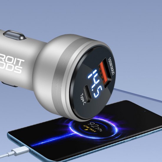 Zilverkleurige autolader met digitale spanningsweergave en type-C poort naast een smartphone