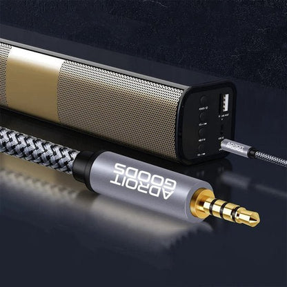 Close-up van een goudkleurige audiokabel met metalen behuizing en zwarte speaker achtergrond