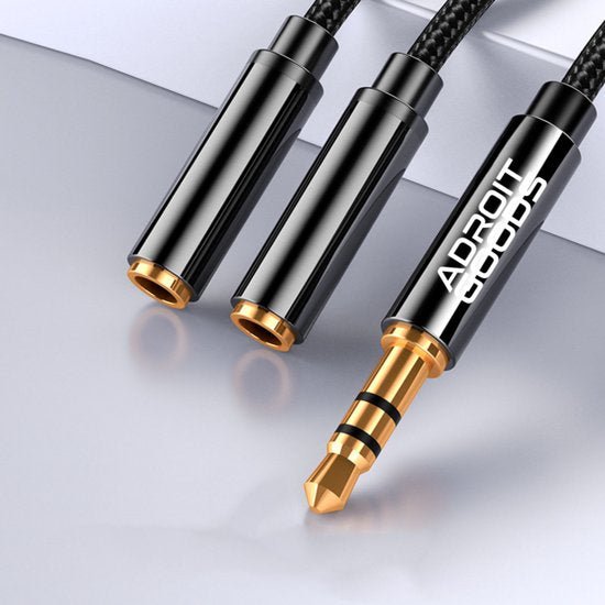 Close-up van een zwarte, gevlochten audiokabel met goudkleurige connectoren en merknaam Adroit Goods