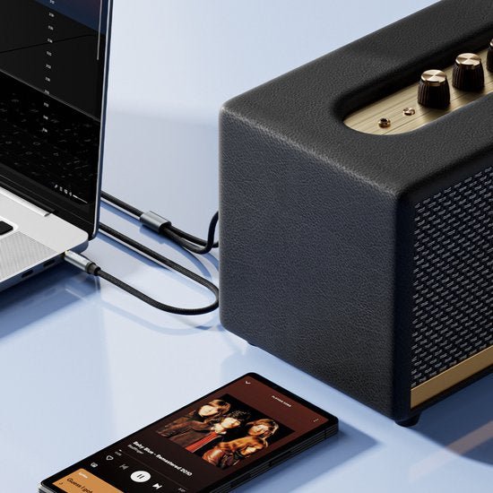 Zwarte luidspreker met gouden knoppen verbonden met laptop en smartphone op tafelhoek