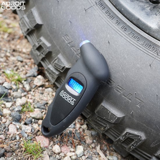 Zwart digitaal bandenspanningsmeter van AdroitGoods bevestigd aan autoband op grindpad