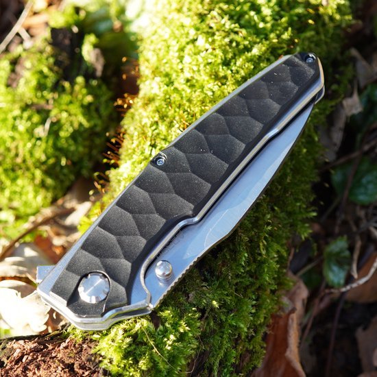 Gesloten zwart grijs inklapbaar mes met metalen details op groene mos achtergrond